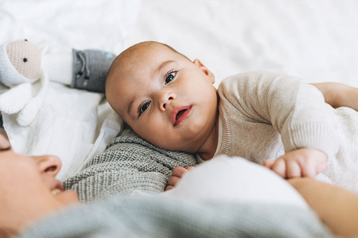 Ernaehrung Saeugling liegt mit Mutter auf dem Bett